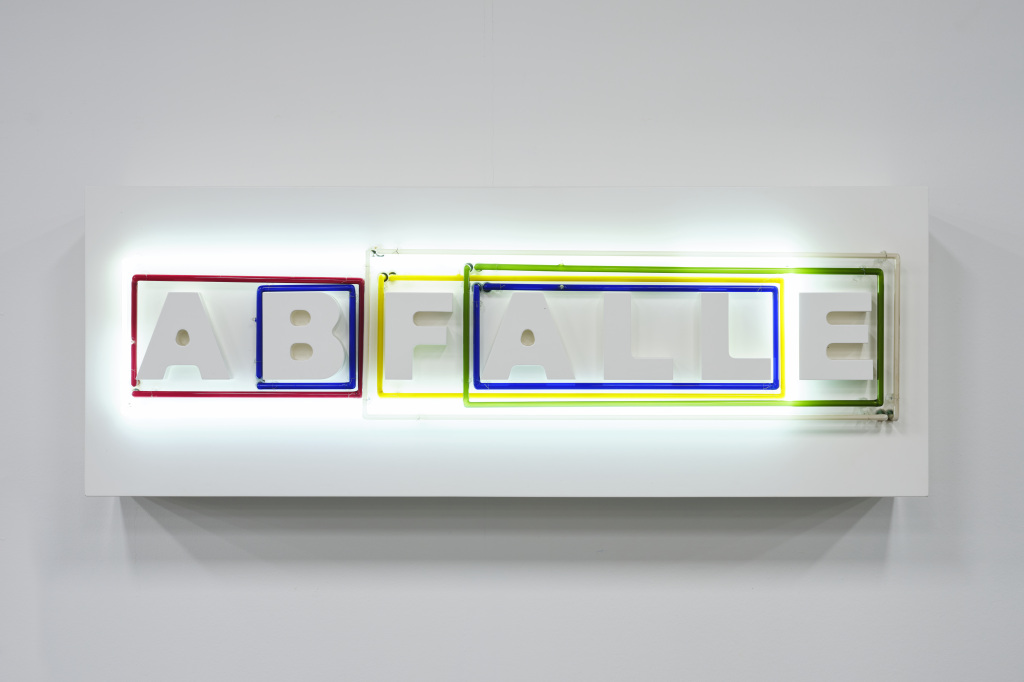 Das Foto zeigt weiße Buchstaben, die das Wort »ABFÄLLE« bilden. Um Buchstabenkombinationen sind Neonröhren in unterschiedlichen Farben und Größen zu sehen. Diese verändern ihre Lichtverhältnisse.
