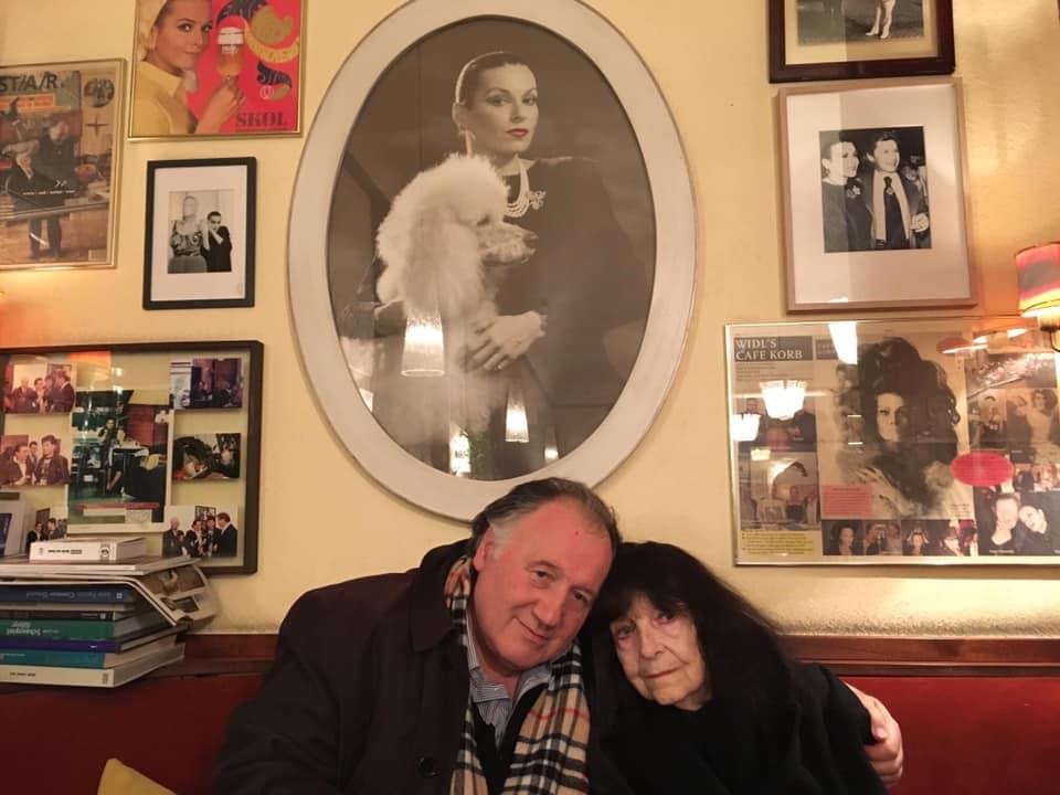 Peter Weibel with Friederike Mayröcker in front of a portrait by Susanne Widl at Café Korb, Vienna 2018.