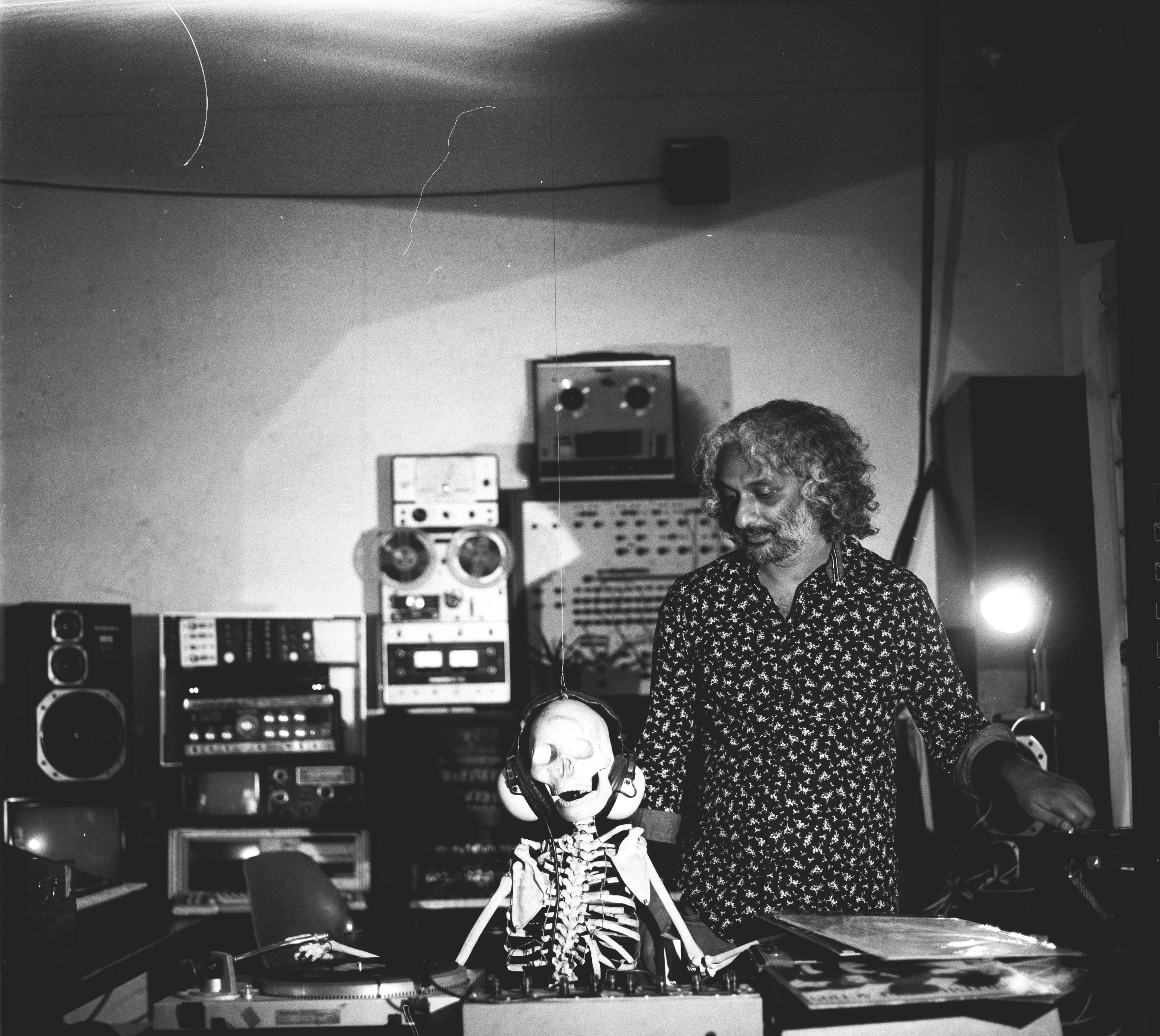 Zu sehen ist Yashas Shetty neben einem Skelett mit Kopfhöhrern auf den Ohren und umgeben von Musikequipment