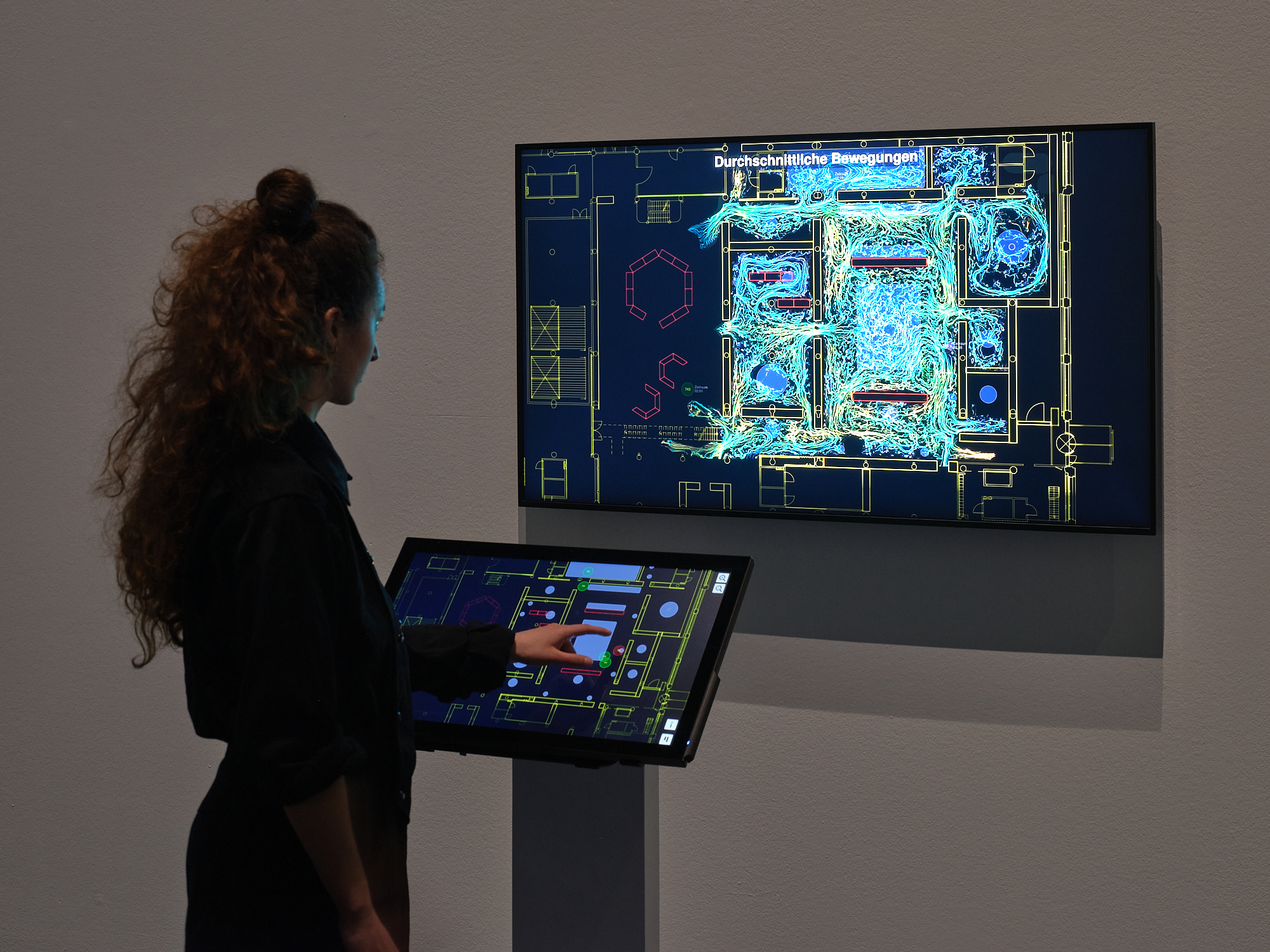 »TRACES« von Bernd Lintermann. Zu sehen ist eine Person vor einem Bildschirm, auf dem verschiedenfarbige Linien abgebildet werden. Vor der Person befindet sich ebenfalls ein Touchscreen-Bildschirm, auf dem sich ebenfalls Linien befinden. 