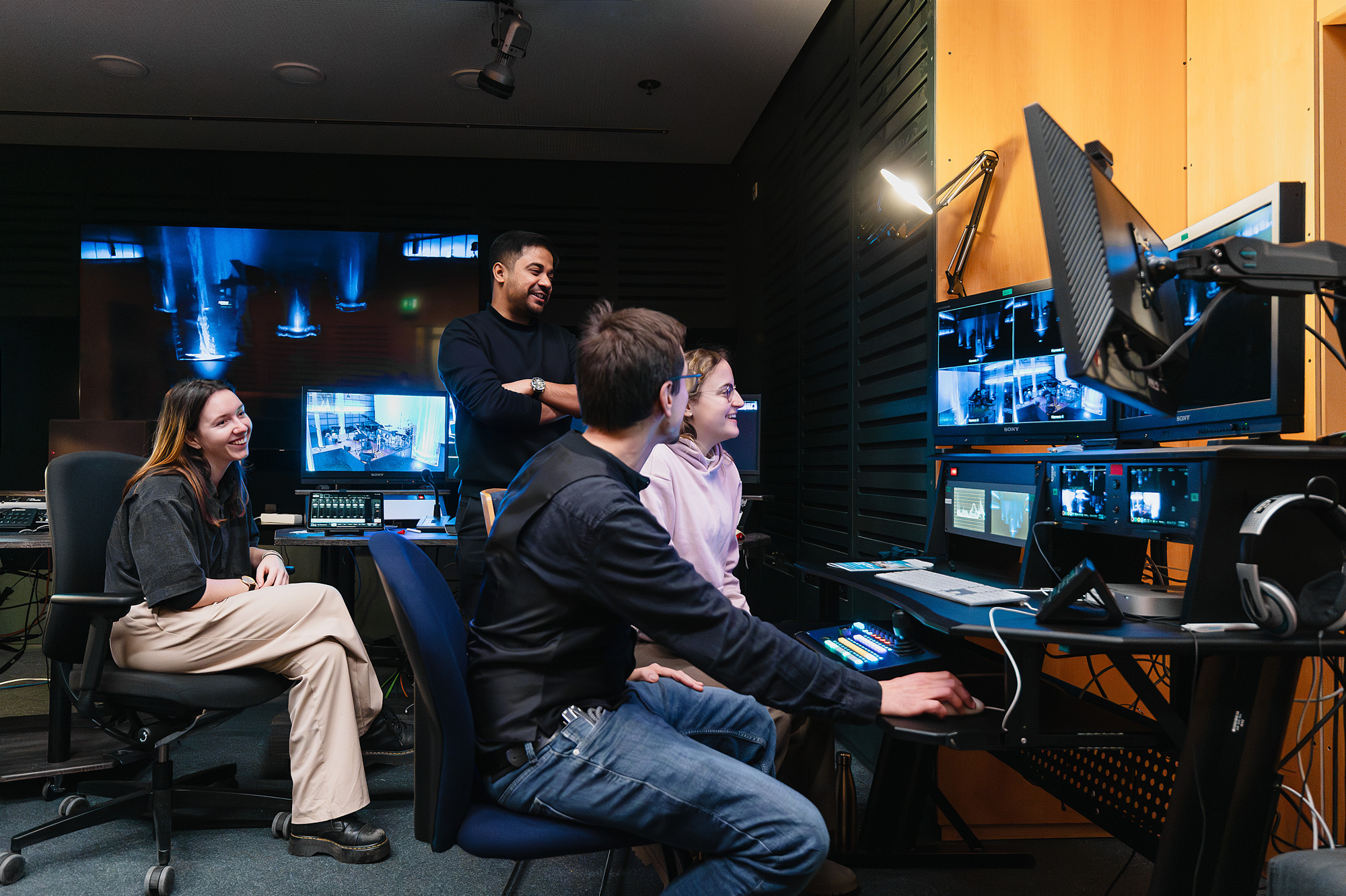 Das Bild zeigt die Mitarbeiter:innen des Videostudios im Regieraum auf Monitore blickend.