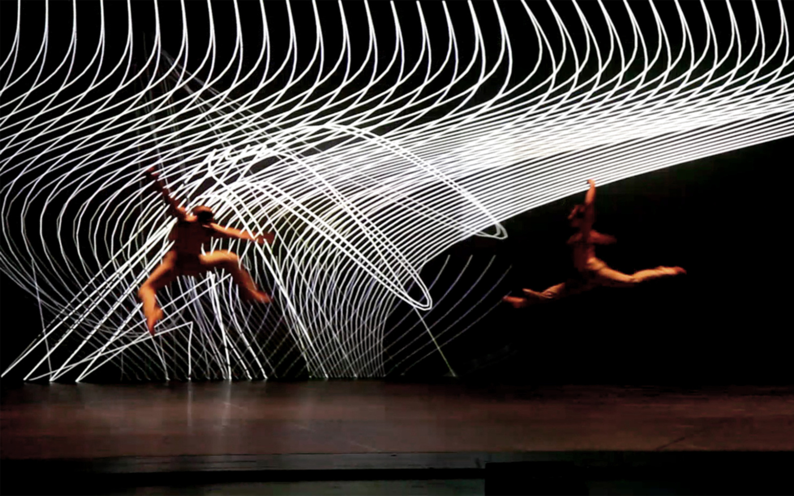 A stage. Two dancers move through the air. In the background spirally white structure.