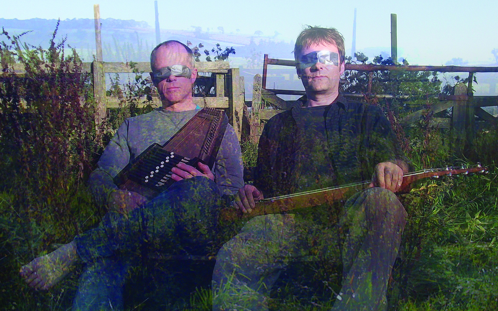 Zwei Männer sitzen mit Musikinstrumenten in der Hand auf einer Wiese, ihre Augen sind mit silbernem Klebeband verhüllt
