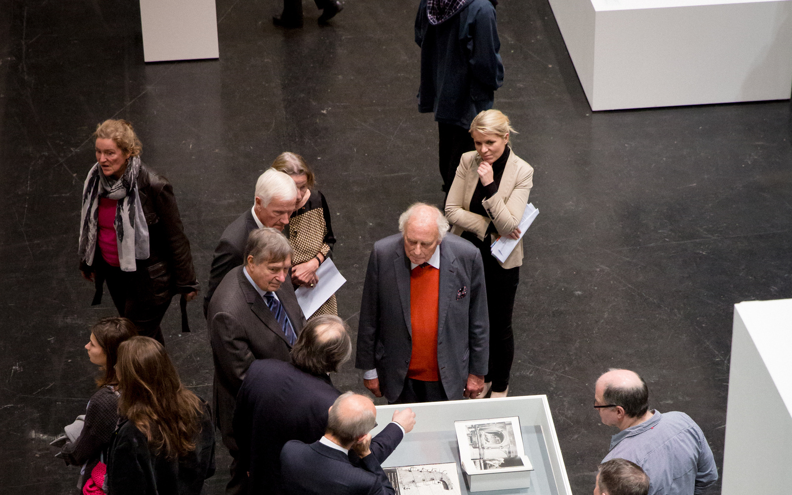 Die Besucher stehen um Herrn Weibel und eine weiße Vitrine, in der mehrere Bücher aufgeschlagen liegen.