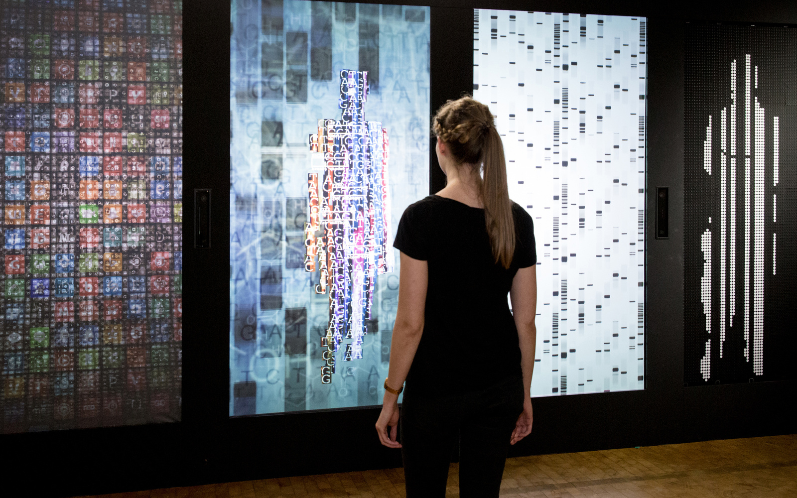 Eine Frau steht vor der Installation YOU:R:CODE, einer Mehrkanalprojektion, die sie in Datenform darstellt