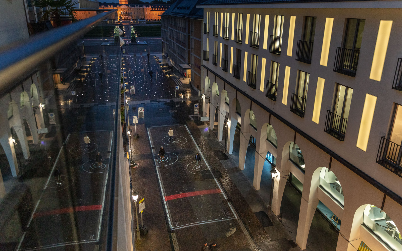 You can see the view of a street from above. On the floor are spiral circles of light. In the background the castle of Karlsruhe is visible. 