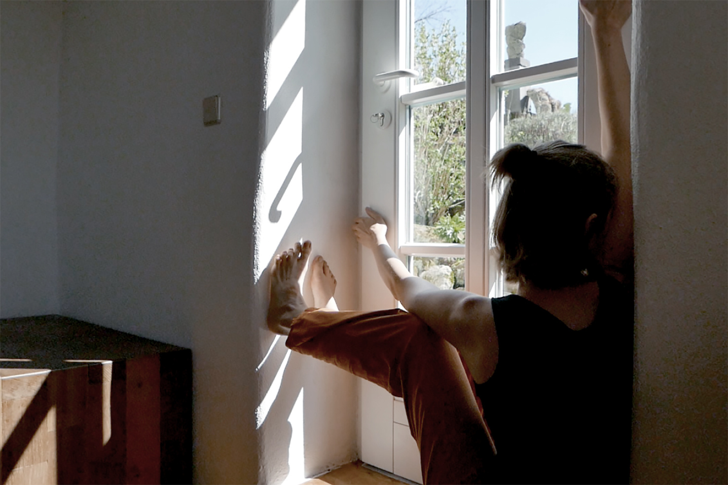 Zu sehen ist eine Person, die auf der Innenseite des Fenstersims sitzt und aus dem Fenster sieht.
