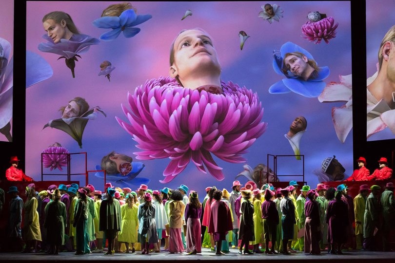 Many people on the stage look up at a screen with projections.