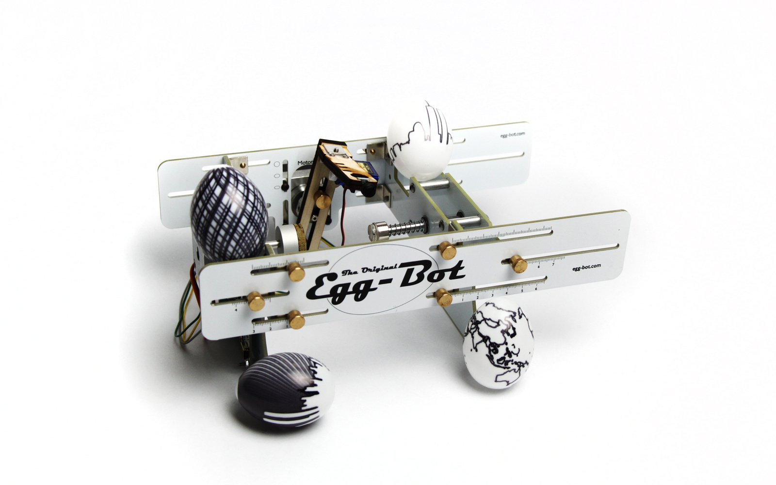 Der Egg-Bot mit vier verschieden bemalten Eieren vor weißem Hintergrund