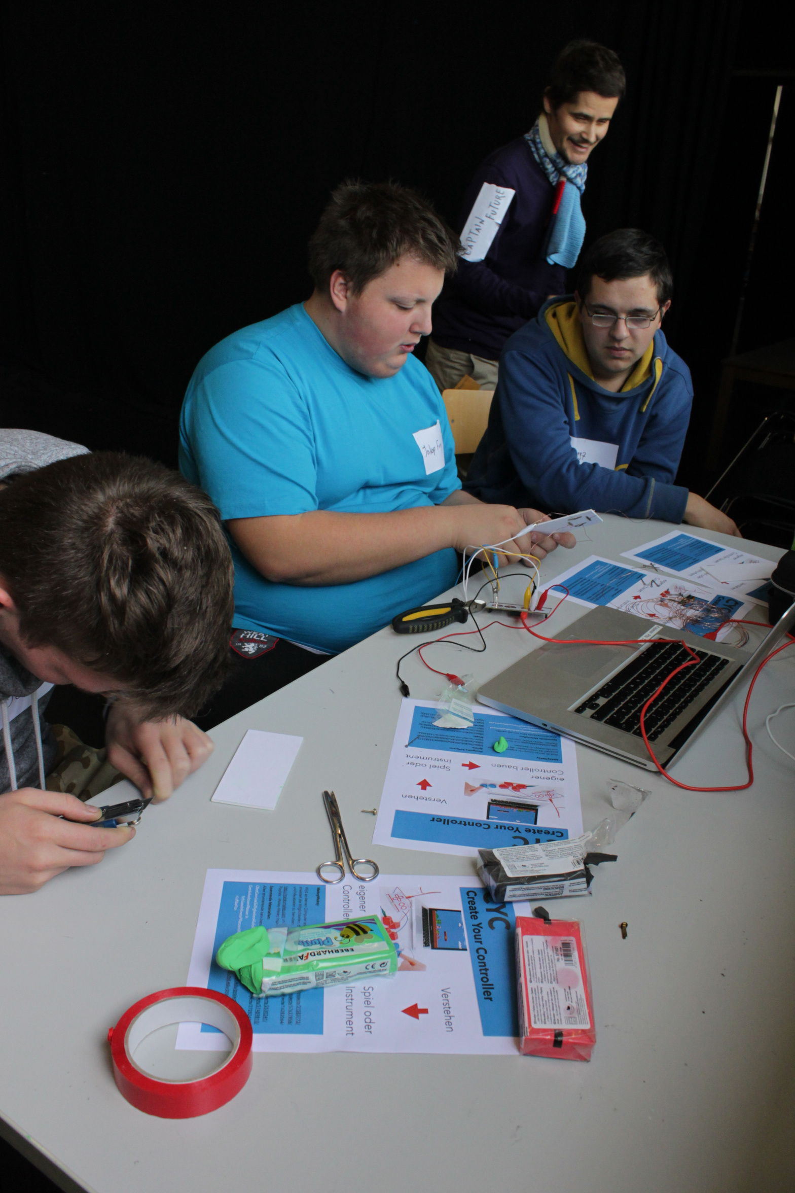 Ein paar Jungen sitzten gemeinsam am Tisch und arbeiten an einem Laptop und dem Bau eines Controllers.