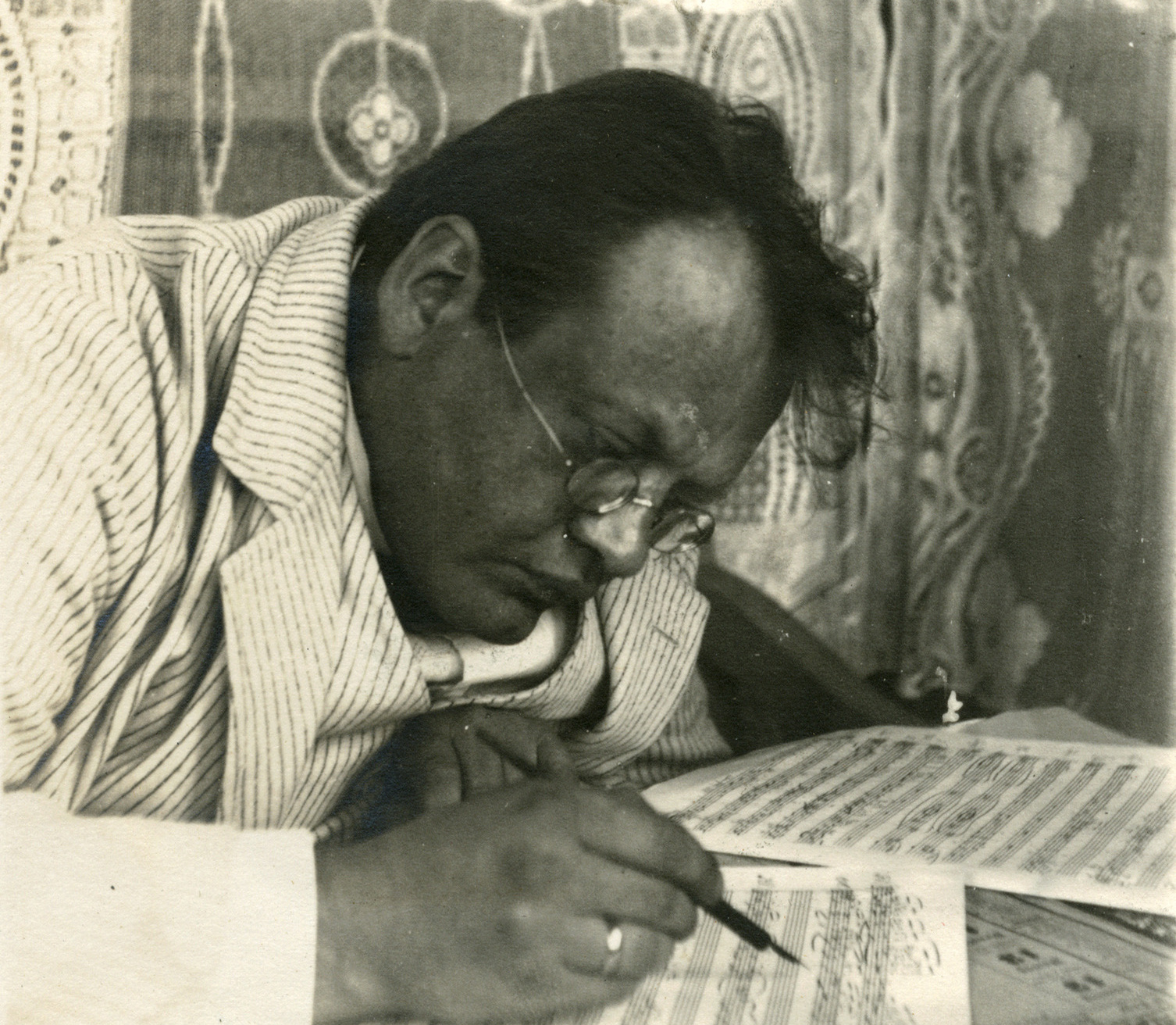 In einer alten schwarz-weiß Fotografie sieht man den Komponisten Max Reger am Tisch gebeugt über Notenblättern sitzen, einen Federhalter in der Hand.