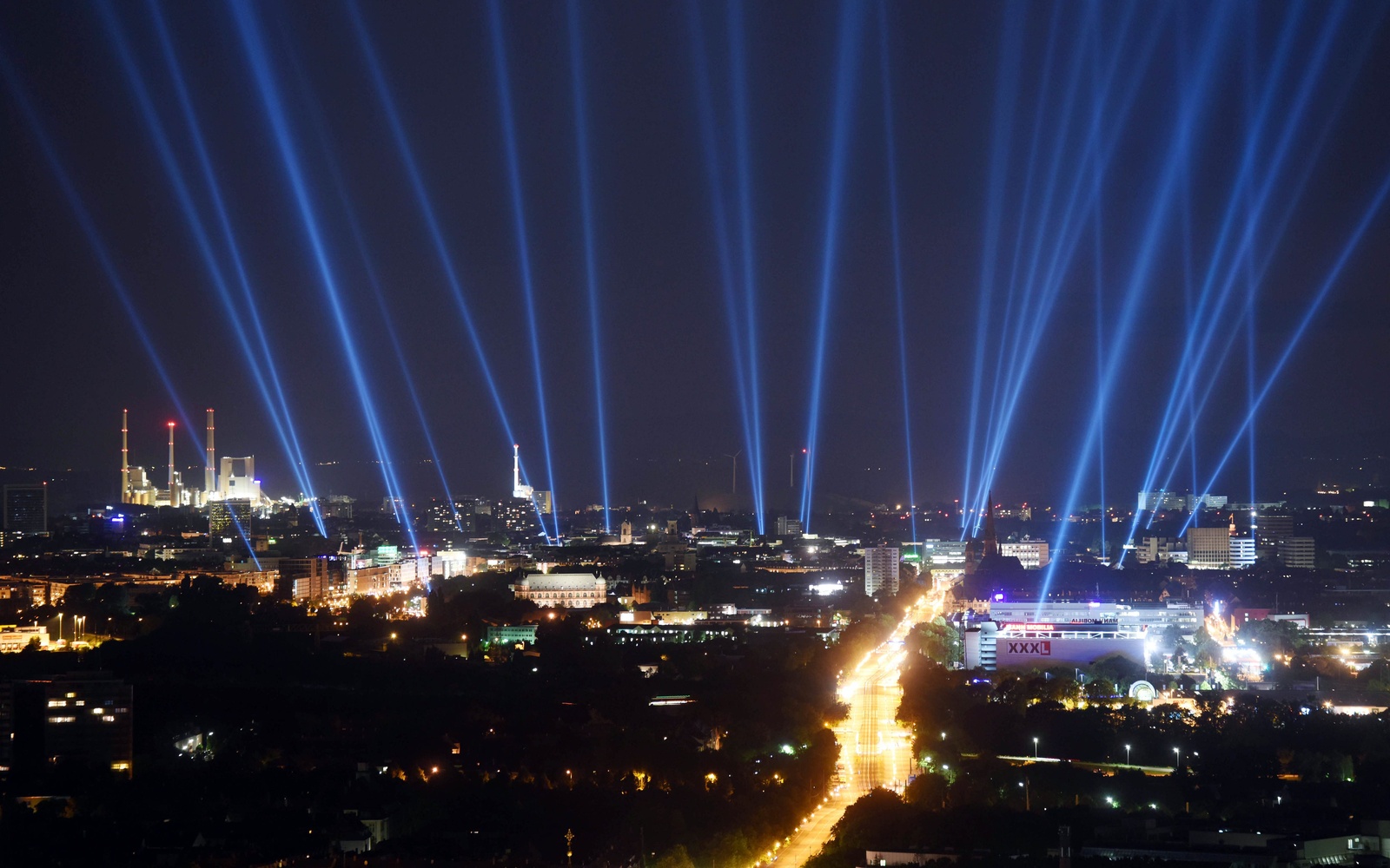 Die Stadt Karlsruhe auf einem Foto bei Nacht, am Himmel sind helle Strahlen zu sehen, die Gebäude der Stadt sind erleuchtet.