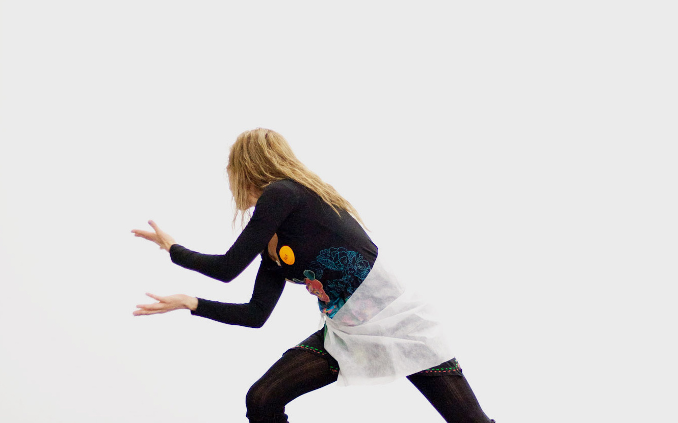 We see a young woman in a dance-like pose. She is leaning on her right leg, that she has flexed. The other one is straight an in one line with her upper body.