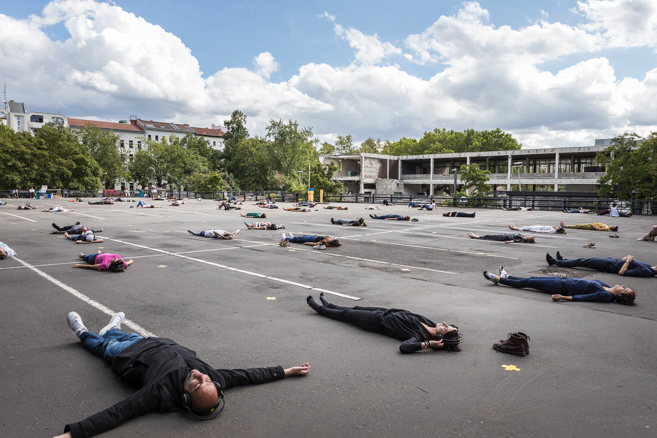 Menschen mit Kopfhörern tanzen in Abstand zueinander auf einem Parkplatz als Teil der Performance »Zerstreuung überall!«
