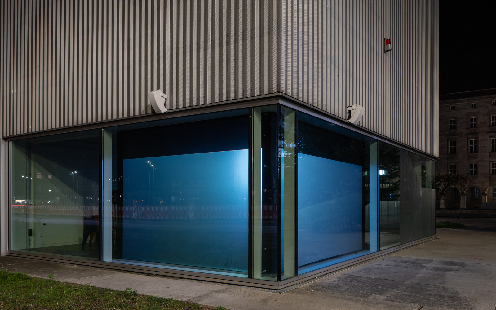 Zu sehen ist eine gläserne Fassade, deren Ecke blau beleuchtet wird
