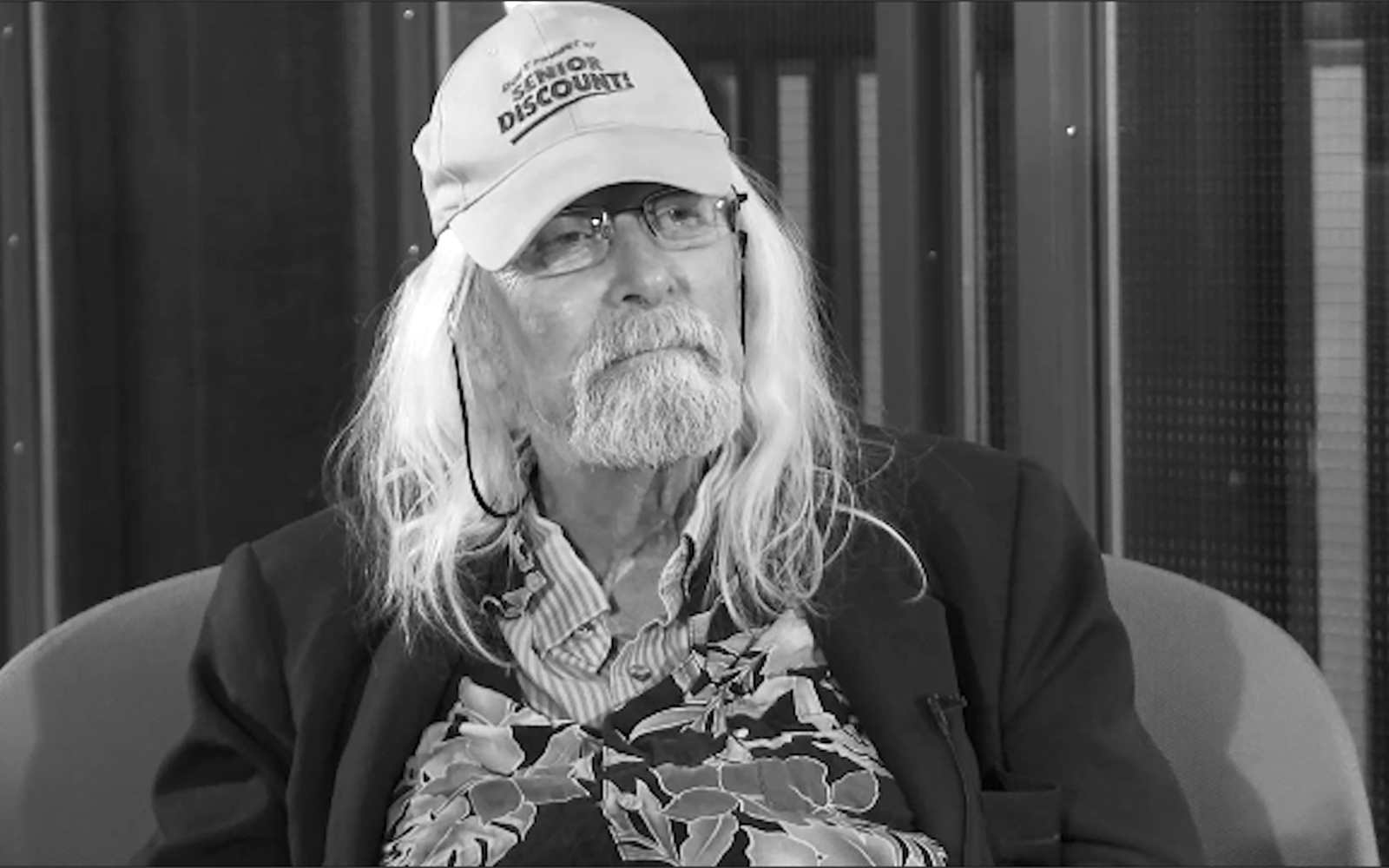 Portrait of Ira Schneider. He wears a baseball cap with the inscription "Senior Discount".