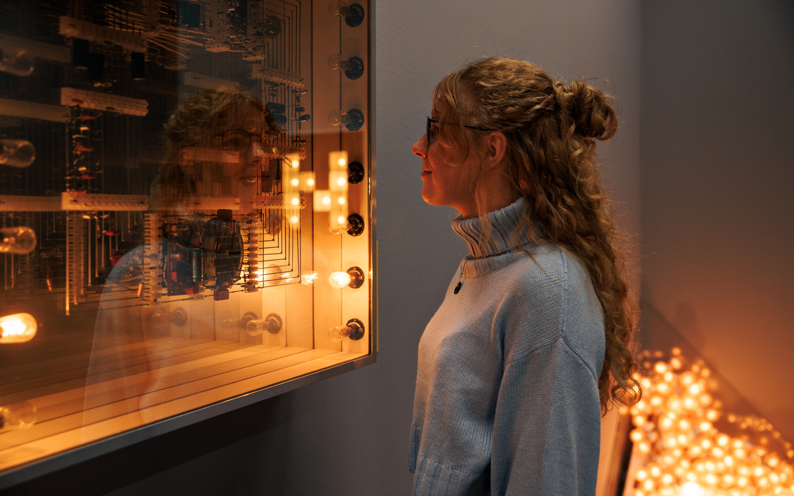 Zu sehen ist eine Person die eine Installation von Walter Giers betrachtet. Zwei der Glühbirnen der Installation leuchten.