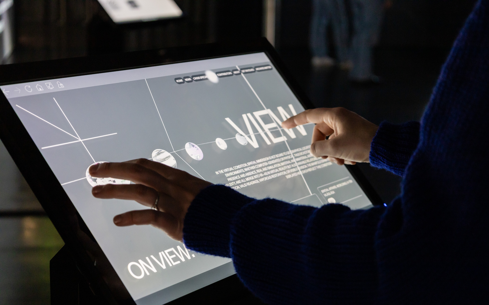 Foto eines Displays in der Ausstellung »Matter. Non-Matter. Anti-Matter«. Auf dem Display steht "View" und es sind kleine planetenartige Symbole zu sehen. 