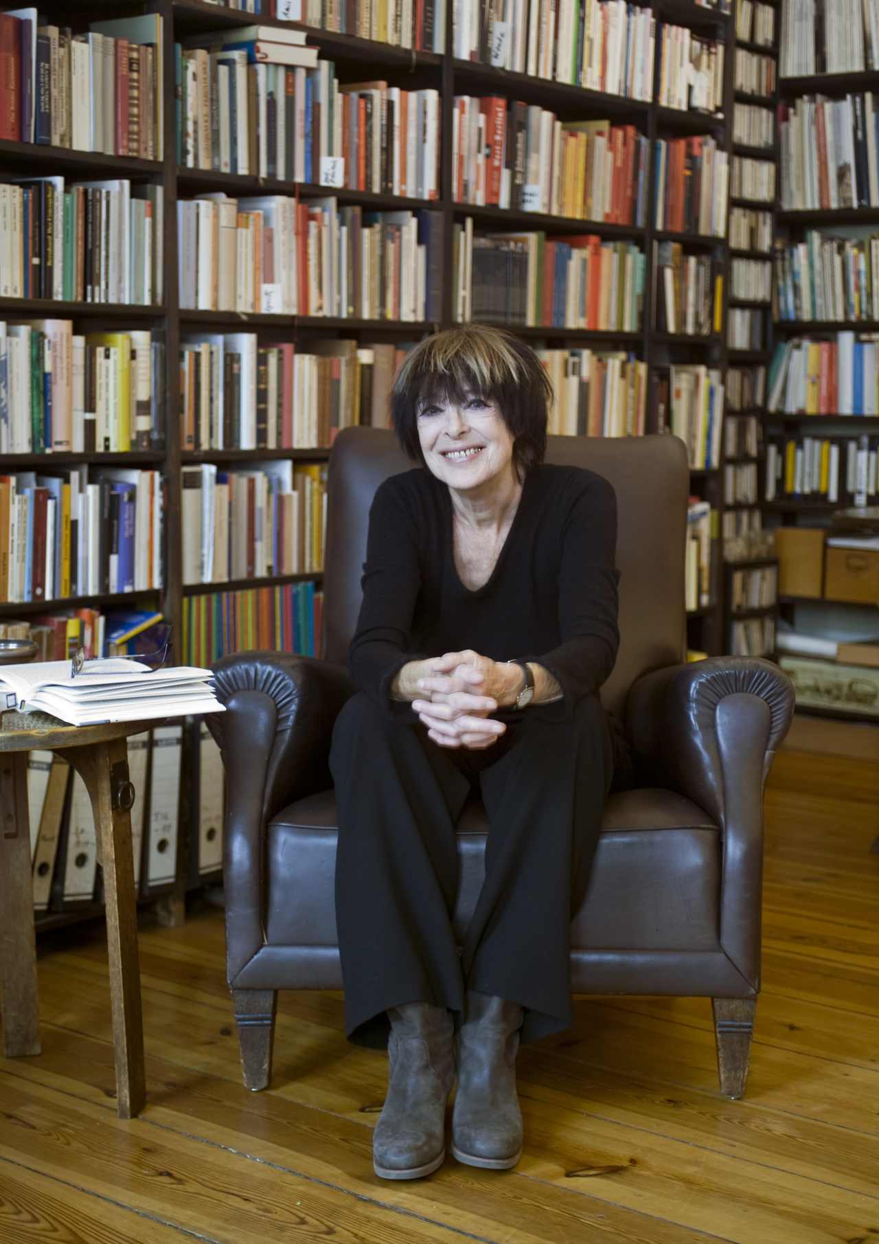 Eine Frau sitzt in einem Sessel vor einem großen Bücherregal.