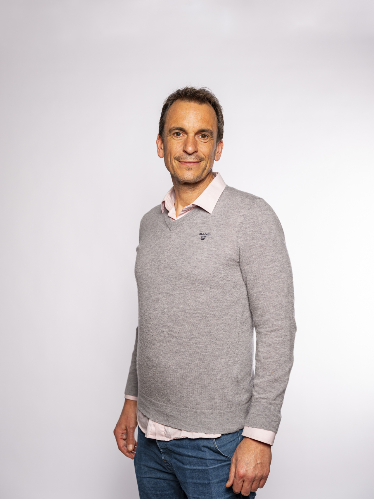 stehender Mann mit hellgrauem Pullover über einem weißen Hemd