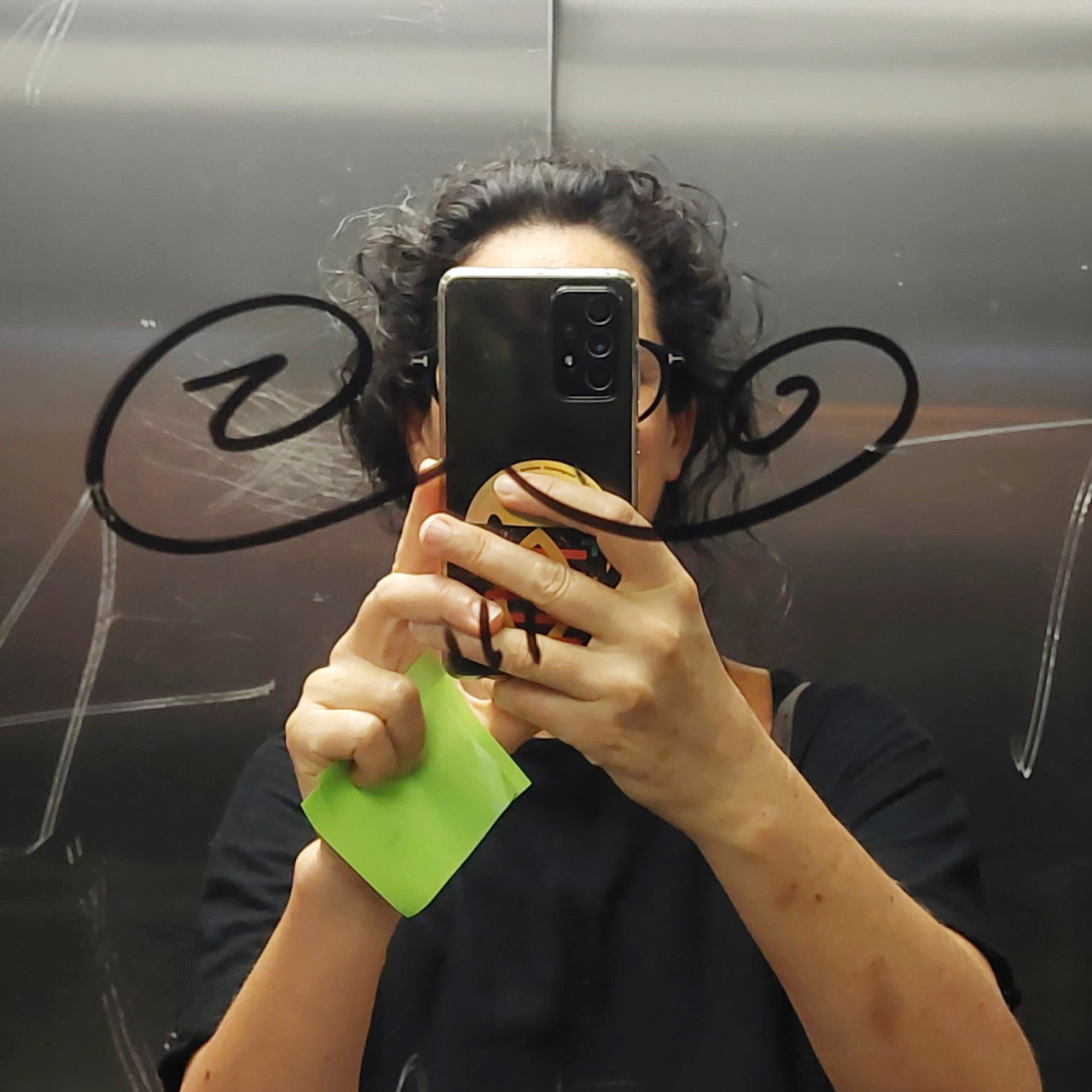 The picture shows a dark-haired woman holding her cell phone in front of her face and taking a selfie in a mirror.