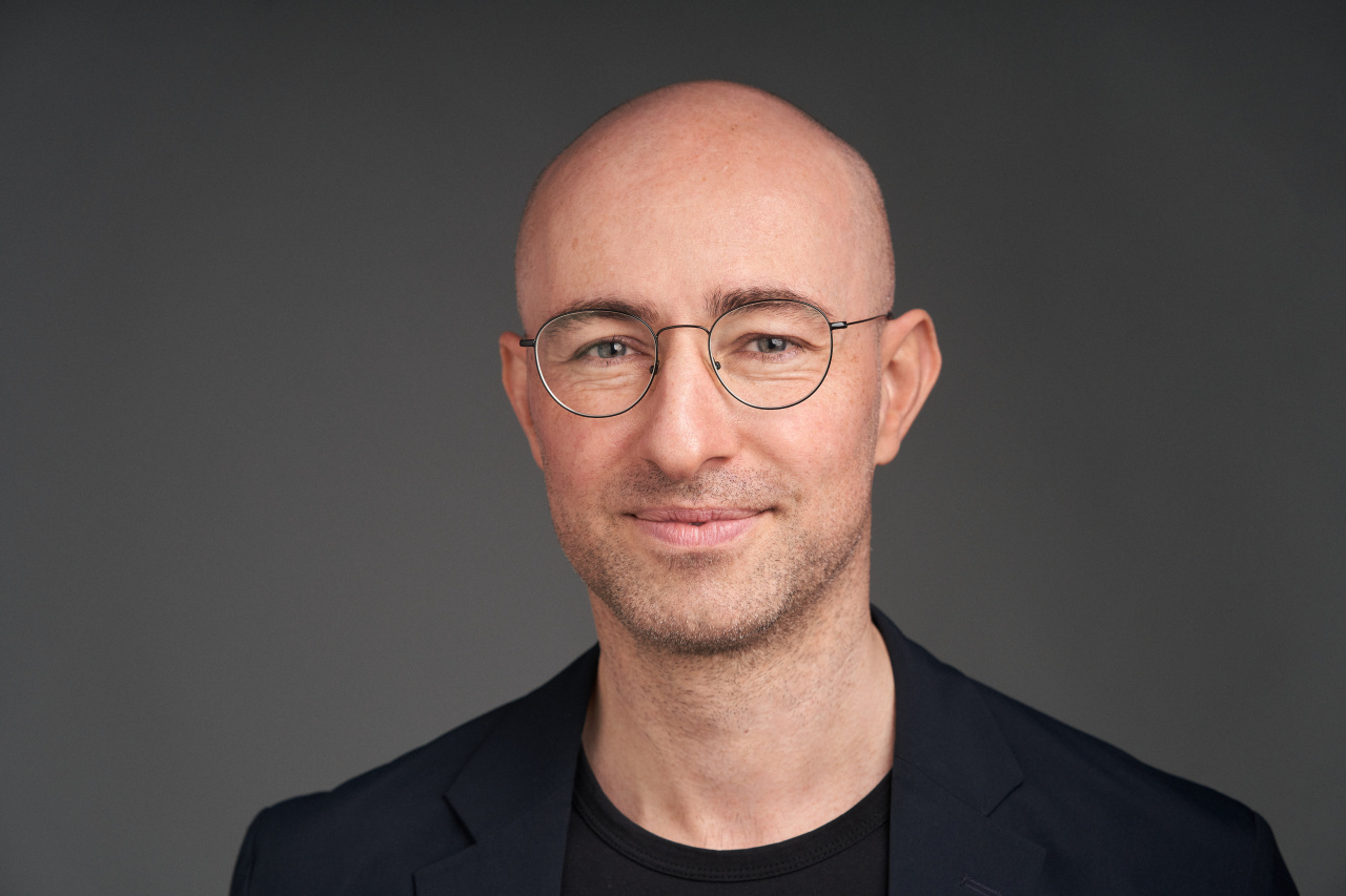 Das Bild zeigt das Portät des Medienkünstlers Alexander Peterhänsel. Er trägt eine Brille und schaut lächelnd in die Kamera.