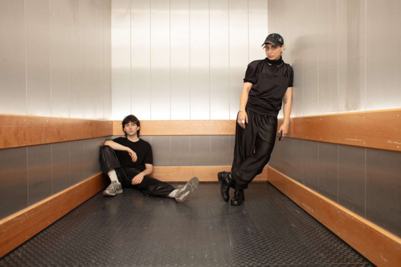 Two people dressed in black are in an elevator.