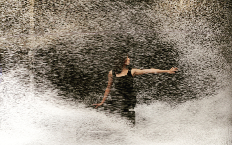 A woman with black hair and a black top moves in a dance-like manner.