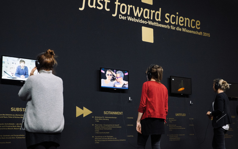 Drei Menschen mit Kopfhörern auf den Ohren schauen verschiedene Videos des »fast forward science 2015« Wettbewerbs an.