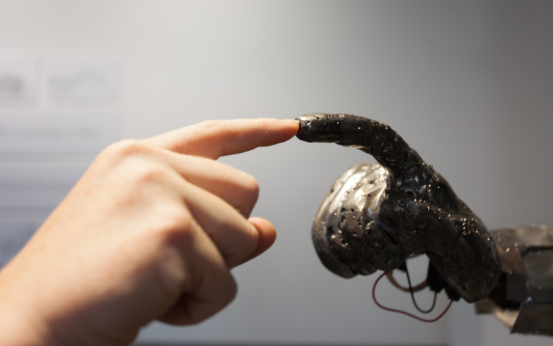 Ein menschlicher Finger berührt den Finger einer Skulptur