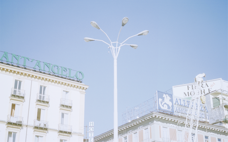 Helle Häuserfassaden und Straßenlaterne vor blauem Himmel.