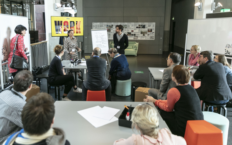 Viele Menschen an Gruppentischen bei einem Workshop