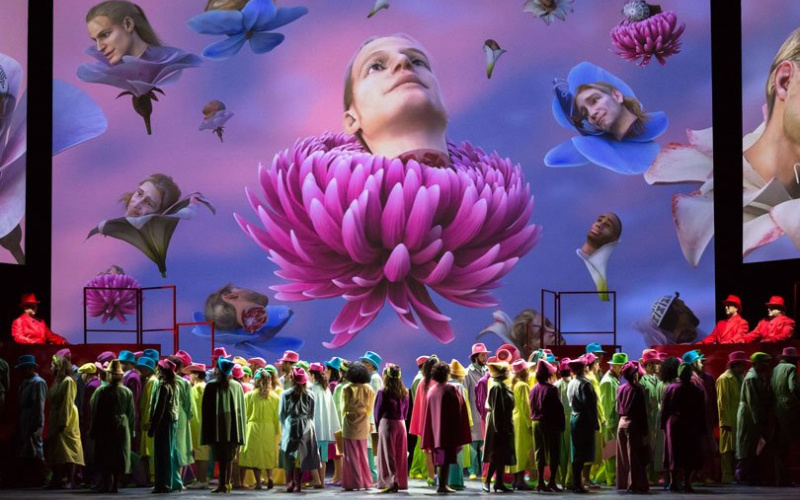 Many people on the stage look up at a screen with projections.