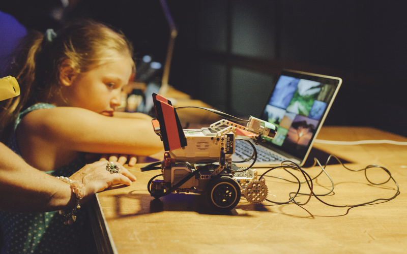 Ein Kind lehnt an einen Tisch, auf dem ein kleiner Roboter steht 