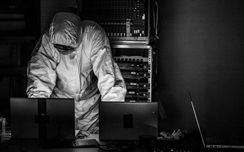 A person in a white protective suit behind a desk with laptops