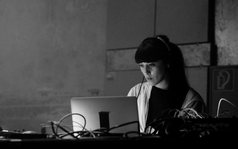 You can see a woman with long hair looking intently at a laptop that is standing in front of her on the desk.