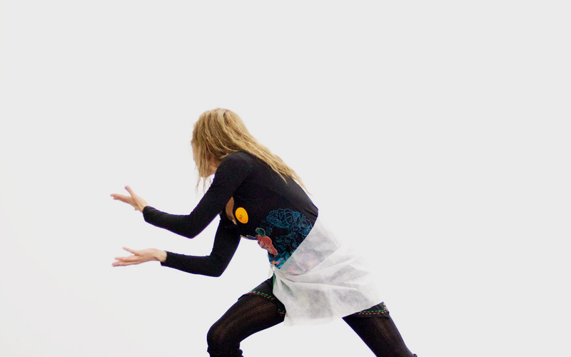 We see a young woman in a dance-like pose. She is leaning on her right leg, that she has flexed. The other one is straight an in one line with her upper body.