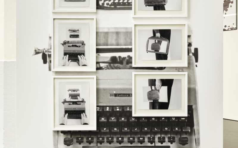 Das Foto zeigt eine schwarz weiße Fotocollage. Der Hintergrund wird von einer alten Schreibmaschine gebildet und auf dieser hängen 6 gerahmte schwarz/weiß Bilder die abwechseln eine Aktentasche und eine Schreibmaschine zeigen.