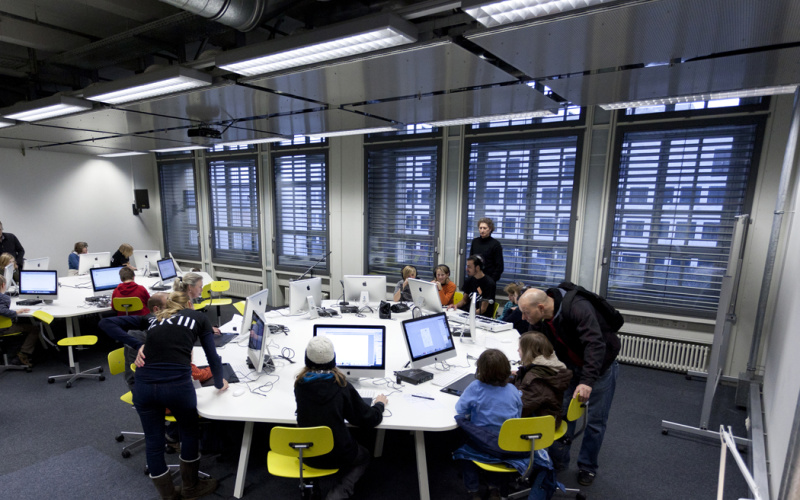 Mehrere Personen sitzen an einem rundem Tisch an Computern