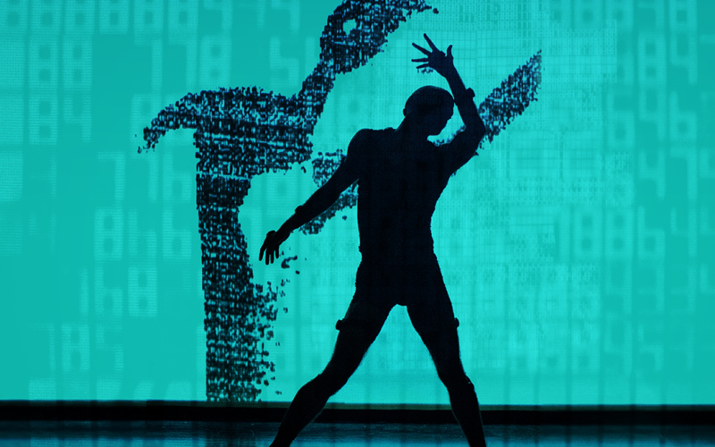The photo shows a stage with turquoise background and black floor, on which the silhouette of a dancing man can be seen, whose shadow is depicted on the back wall.