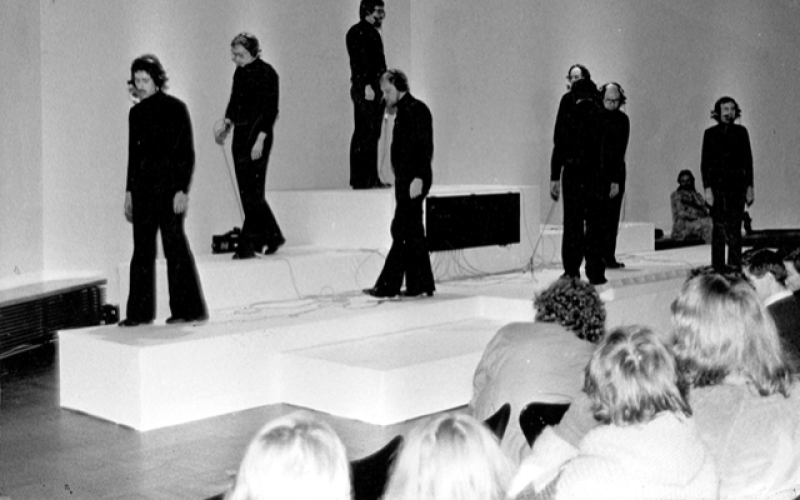 »Homo lusus – der gespielte Mensch« von Walter Giers. Es sind neun in schwarz bekleidete Personen zu sehen, die auf Podesten stehen. 