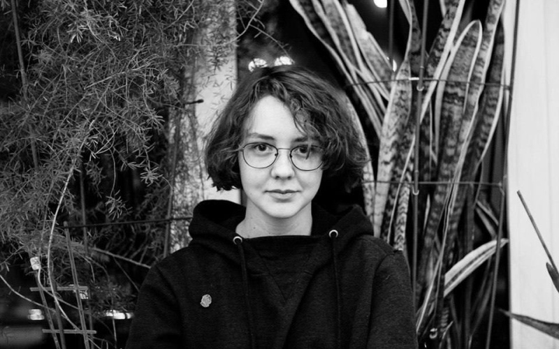 The picture shows the young curator Natasha Chychasova. It is a black and white portrait and she smiles frontally into the camera.