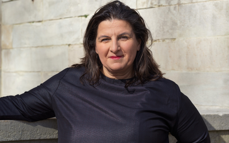 Portrait of Çağla Ilk in a black dress in front of a white stone wall 