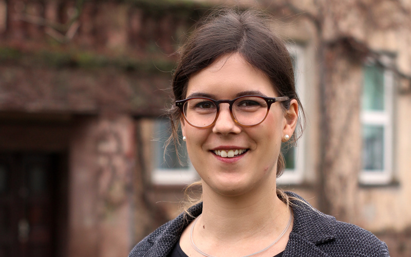Eine Frau mit Brille, braunen Haaren und einem Blazer.