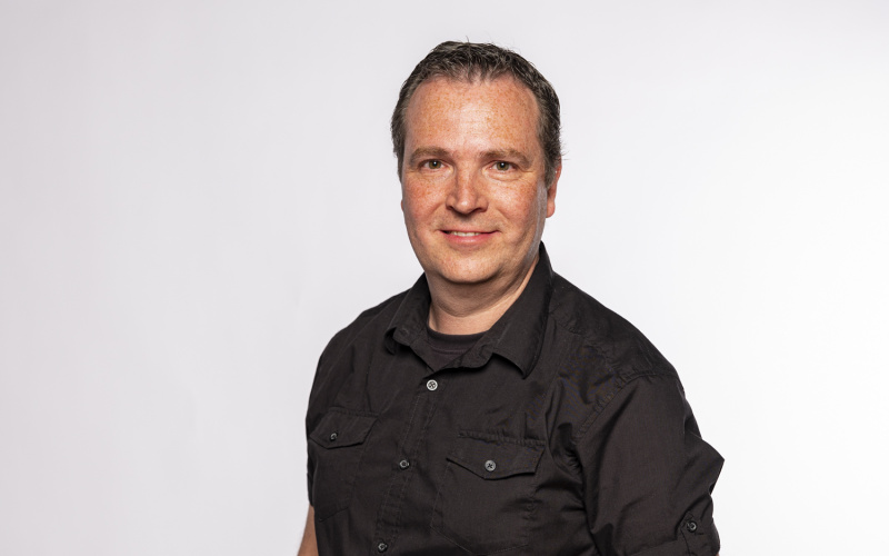 stehender Mann mit schwarzem Hemd und die Hände in der Hosentasche