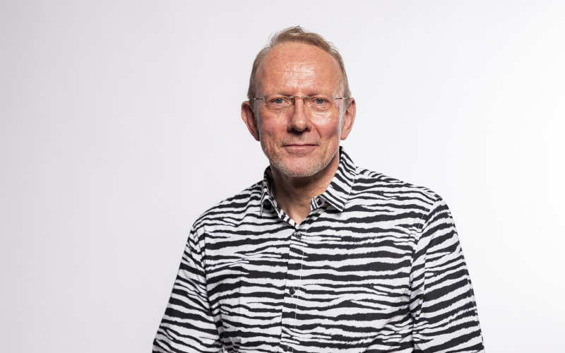 seated man with light-colored hair and a white and black patterned shirt