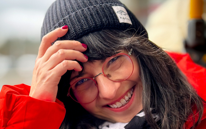 A smiling woman in a woolly hat wearing a thick red jacket.