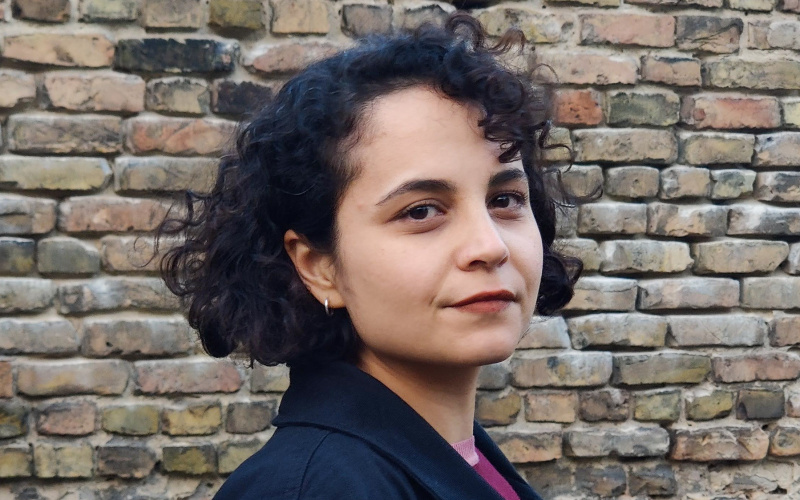 Portrait of a woman with black curls and a purple top.