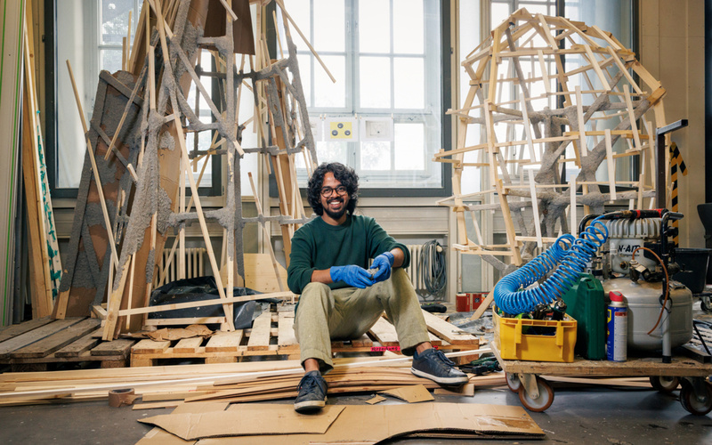 Ein Mann mit schwarzen Locken arbeitet an seinem Kunstwerk aus Holzlatten.