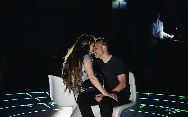 Two people are sitting in front of a black background, kissing.